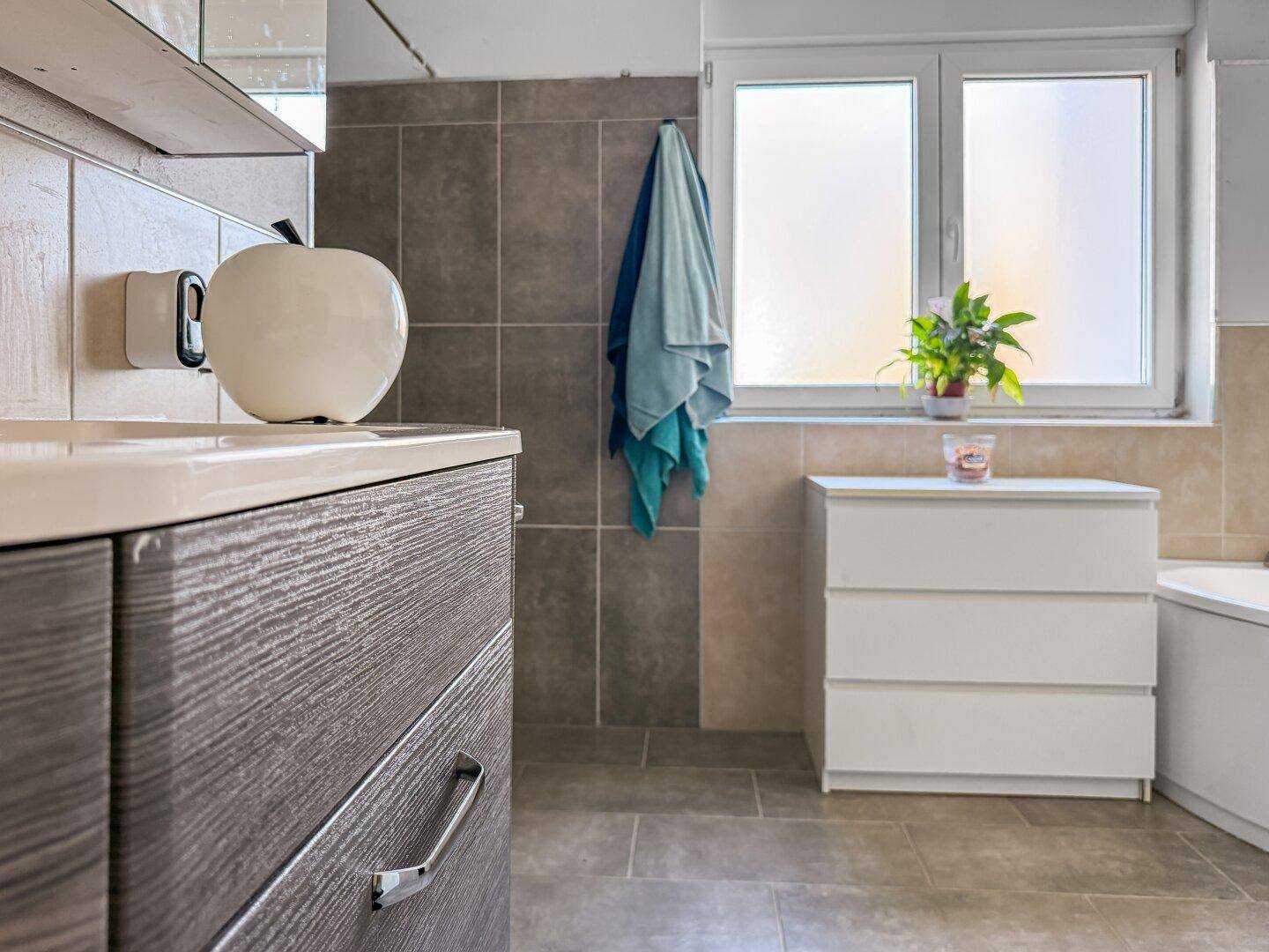 Detailansicht des Badezimmers mit Waschtisch, Spiegelschrank und Eckbadewanne.