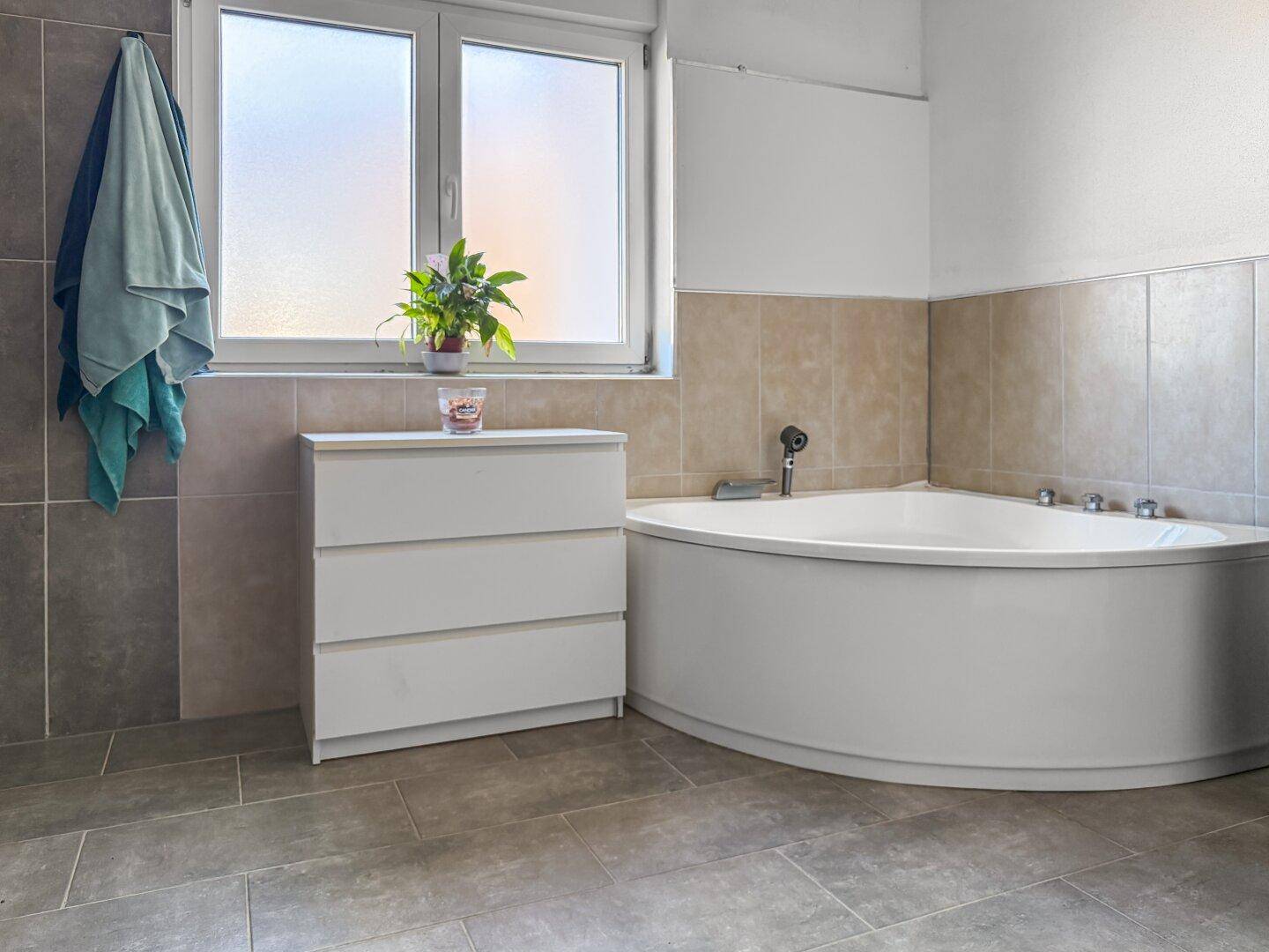 Geräumiges Badezimmer mit Eckbadewanne, Fenster und hellen Fliesen.