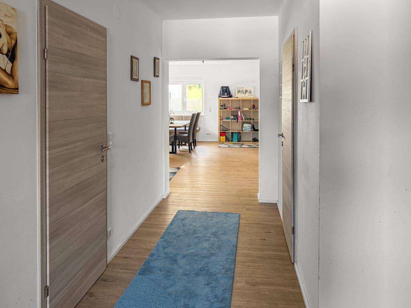Langer Flur mit Laminatboden, Holztüren und Blick in den Wohnbereich.