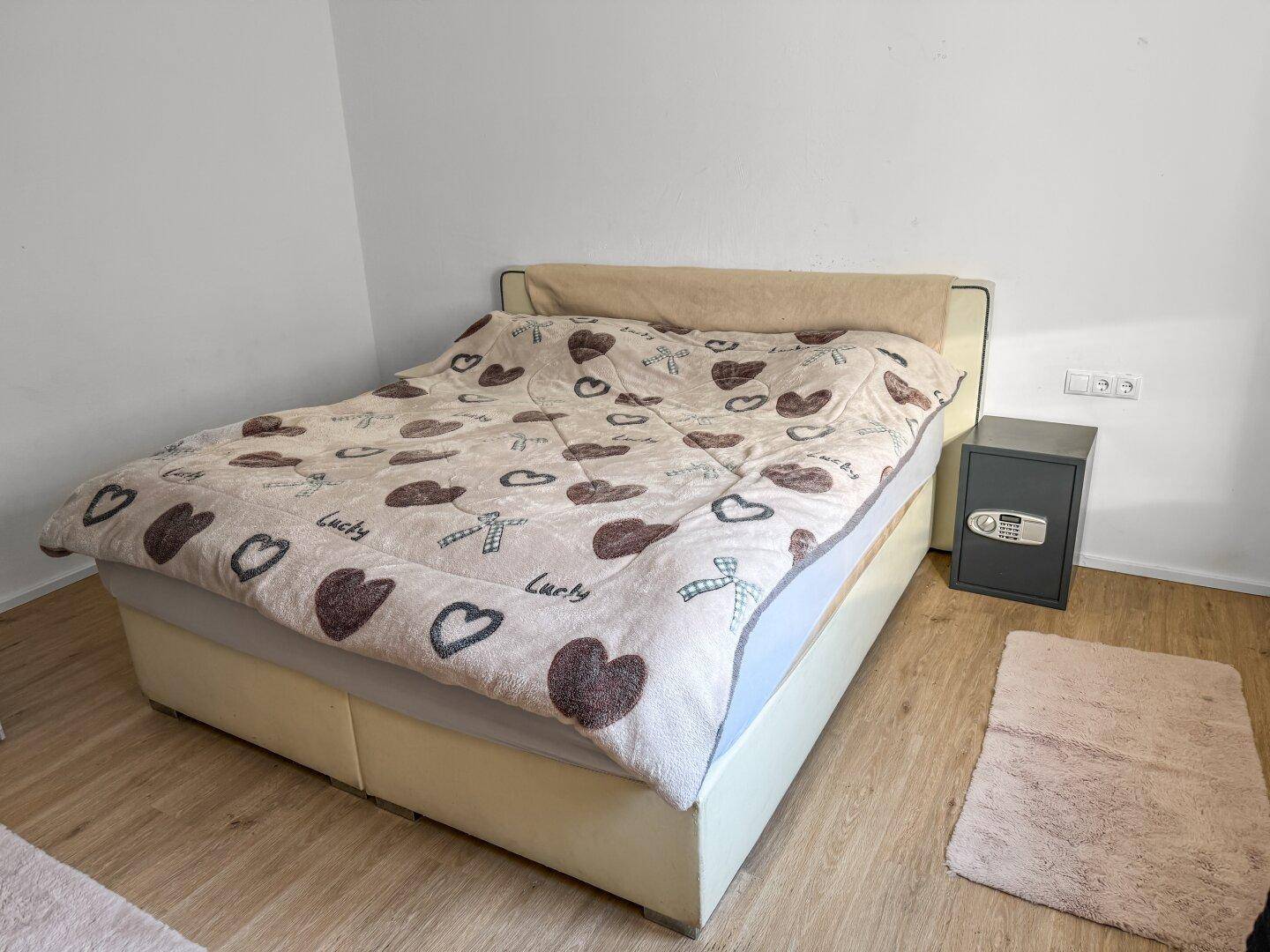Schlafzimmer mit Doppelbett, Safe und hellem Laminatboden.