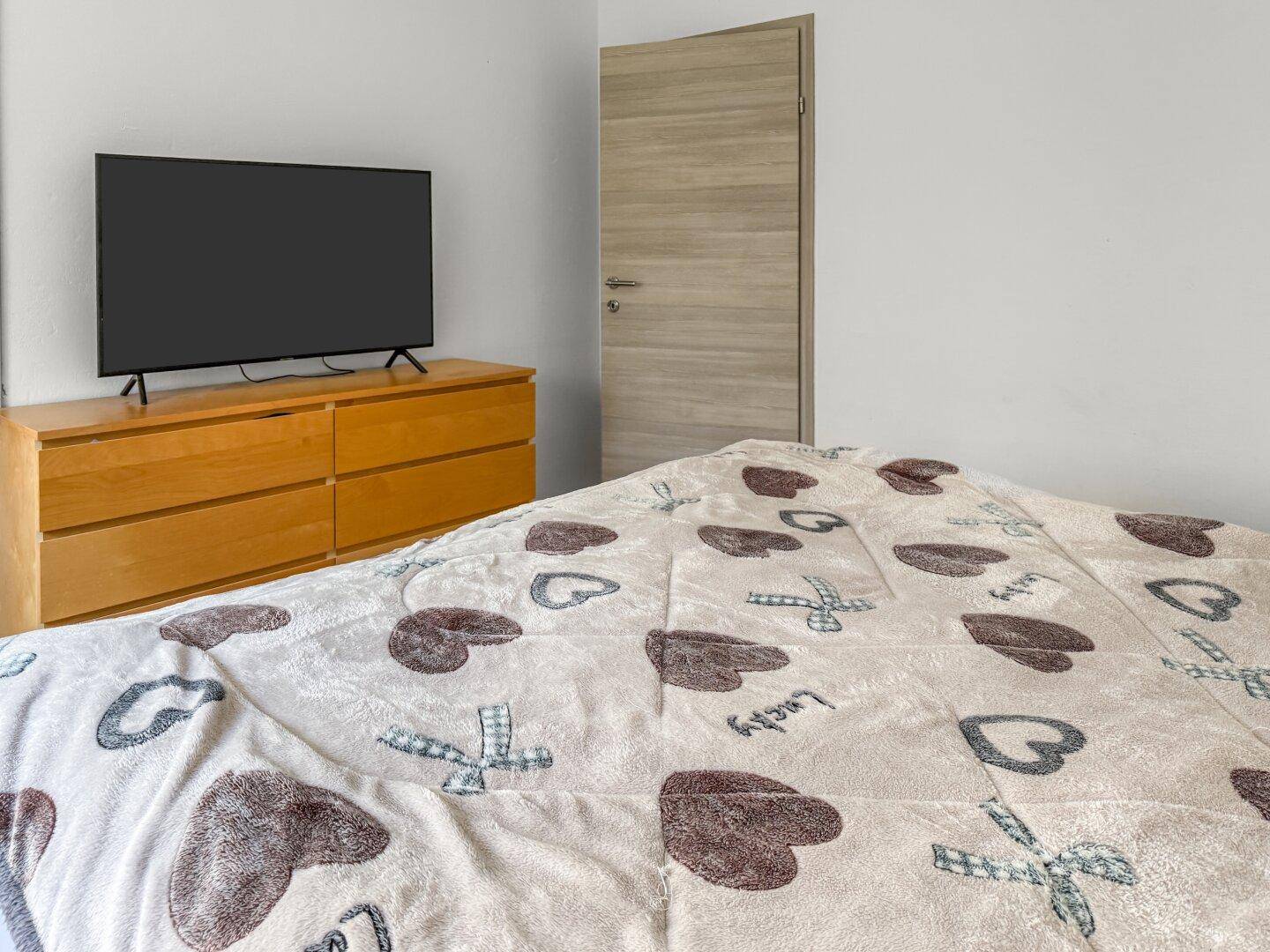 Schlafzimmer mit Doppelbett, Kommode und Fernseher.