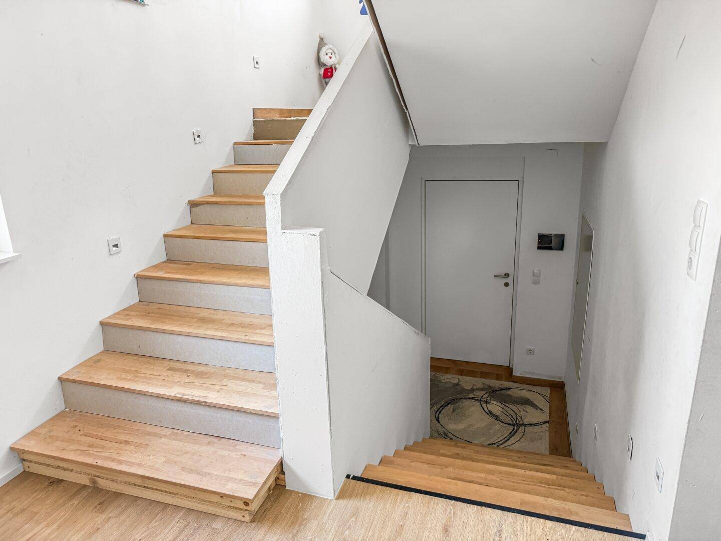 Heller Treppenaufgang mit Holzstufen und weißem Geländer.