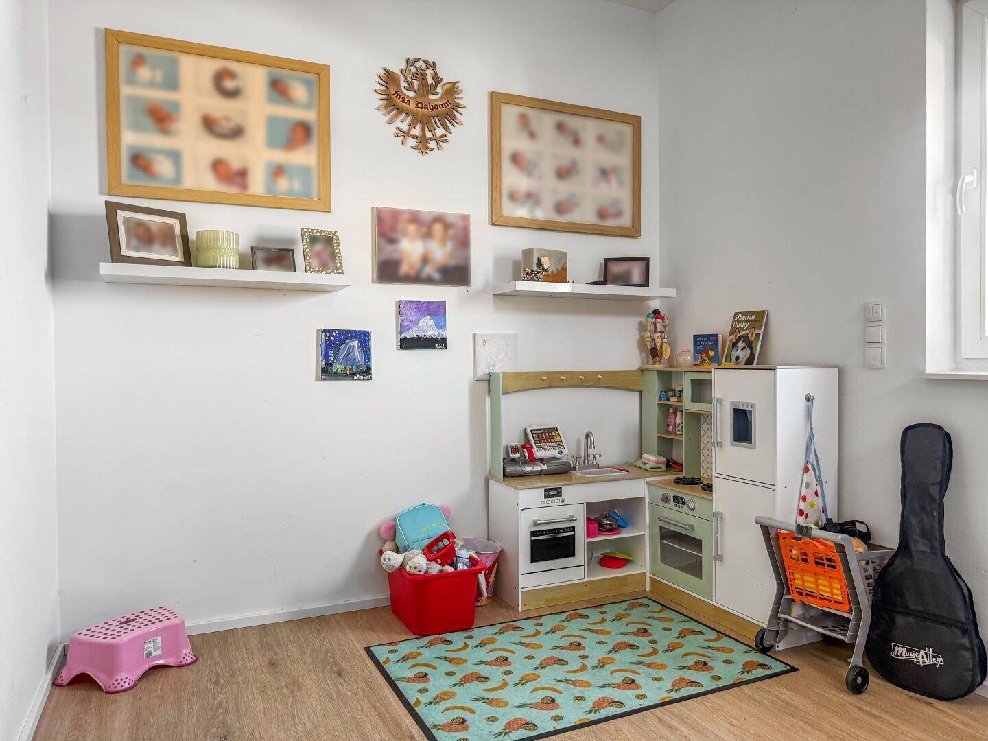 Kinderzimmer mit Spielküche, Teppich und bunten Dekorationen.
