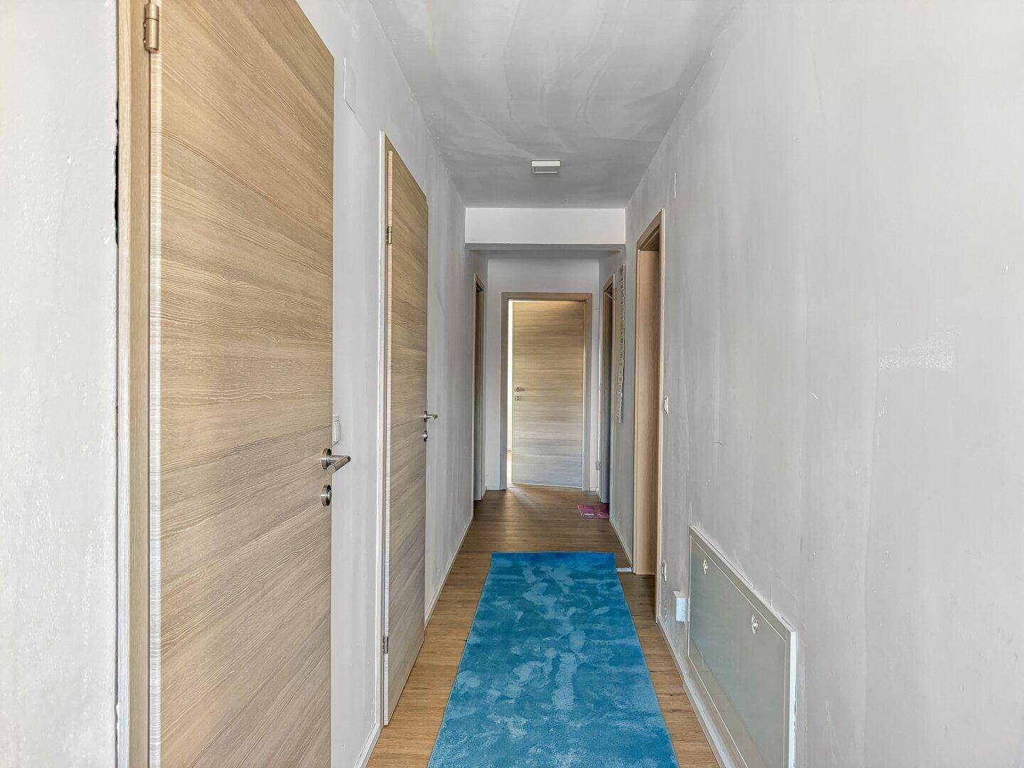 Langer Flur mit Holztüren und blauem Teppichläufer.