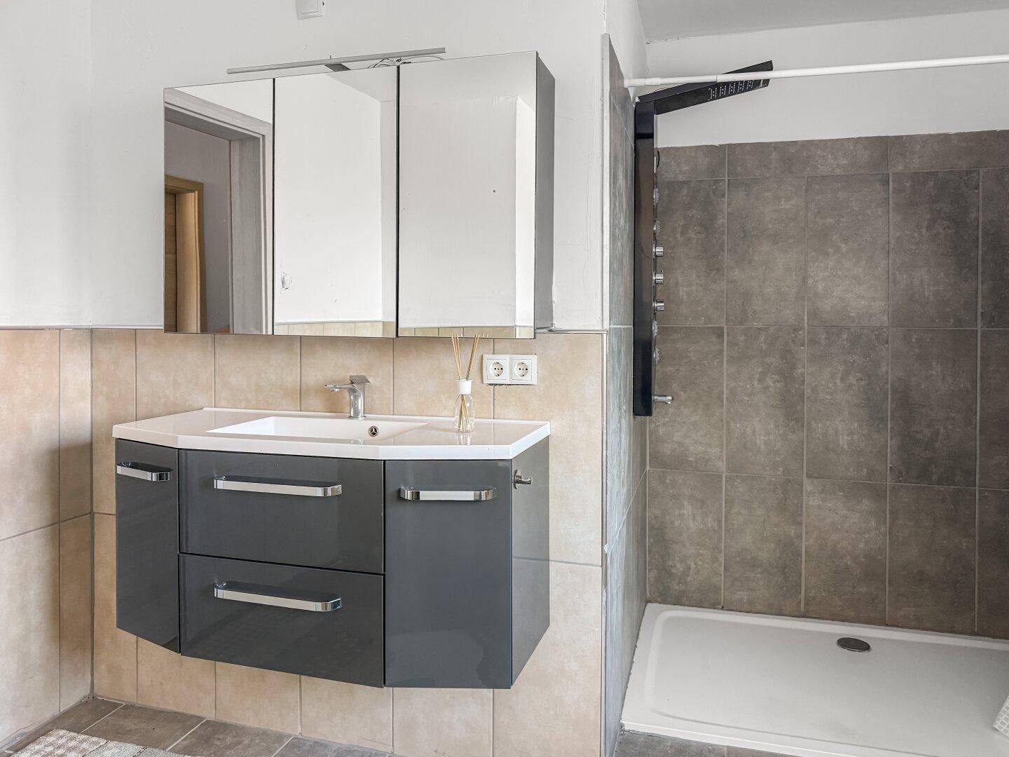 Modernes Badezimmer mit Duschkabine, Waschtischunterschrank und Spiegelschrank.
