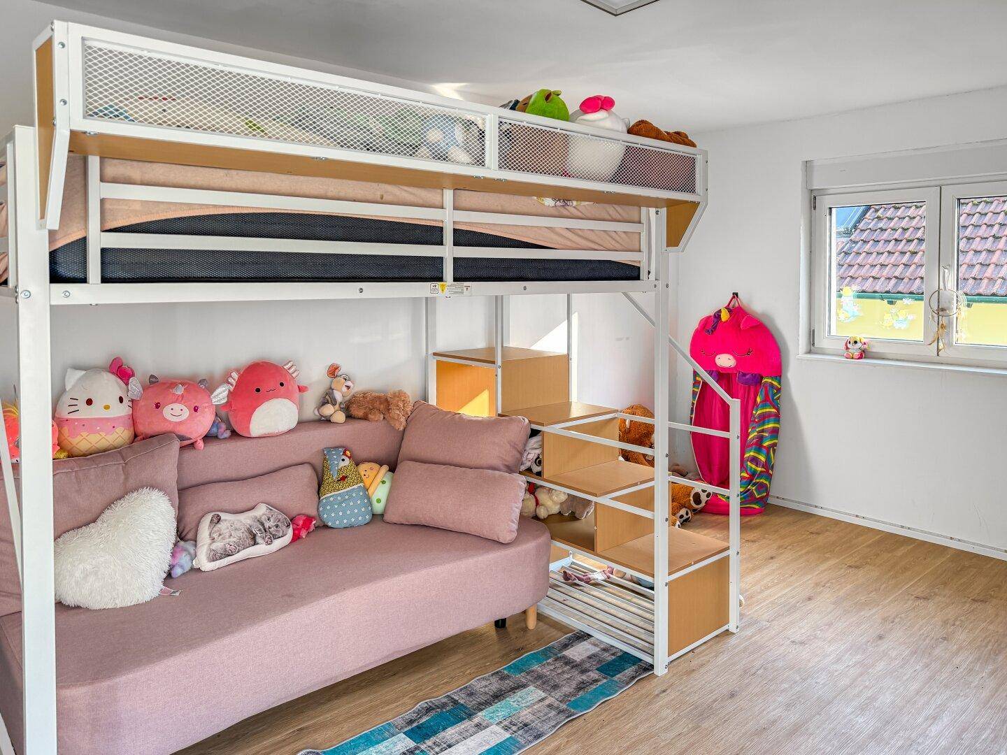 Kinderzimmer mit Hochbett, Sofa und Fenster mit Blick ins Grüne.