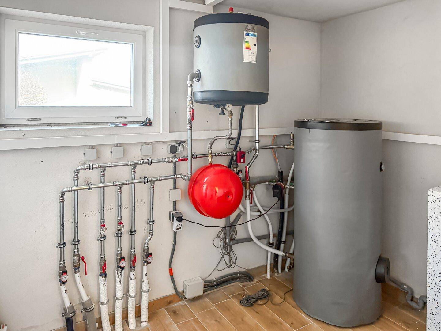 Heizungsraum mit Warmwasserspeicher, Verteiler und Fenster.
