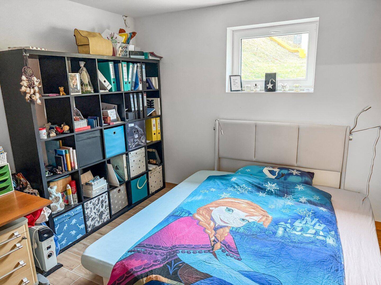 Schlafzimmer mit Bett, Regal und Fenster mit Blick ins Grüne.