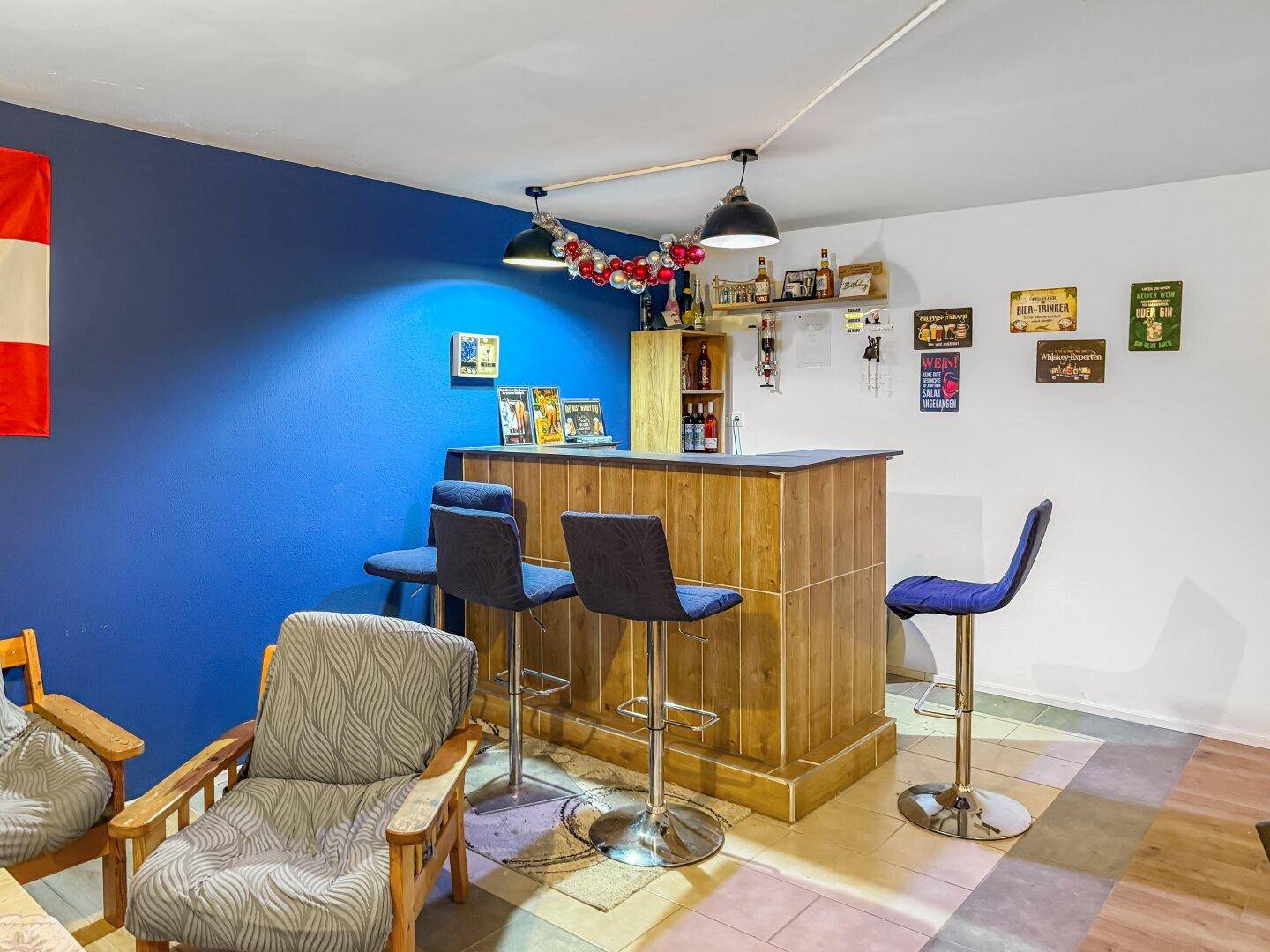 Kellerbar mit Holzverkleidung, Barhockern und blauer Wand.