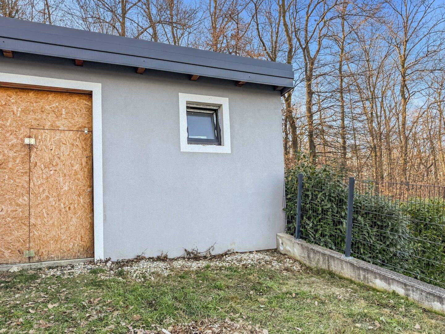 Kleines Nebengebäude im Garten mit Fenster und Holztür.