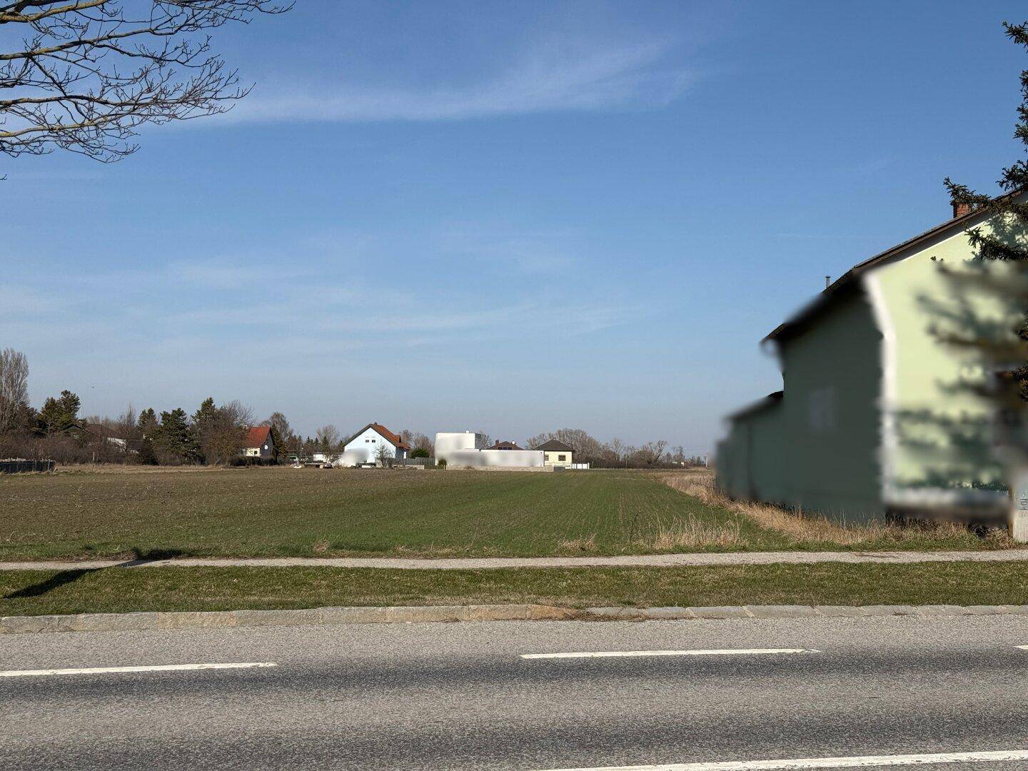 Blick über ein weites Feld mit einer Straße im Vordergrund und Häusern in der Ferne.