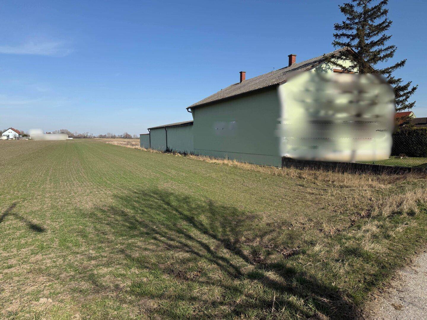Weitläufiges Feld neben einem Gebäude, mit einem Weg im Vordergrund und ländlicher Umgebung.