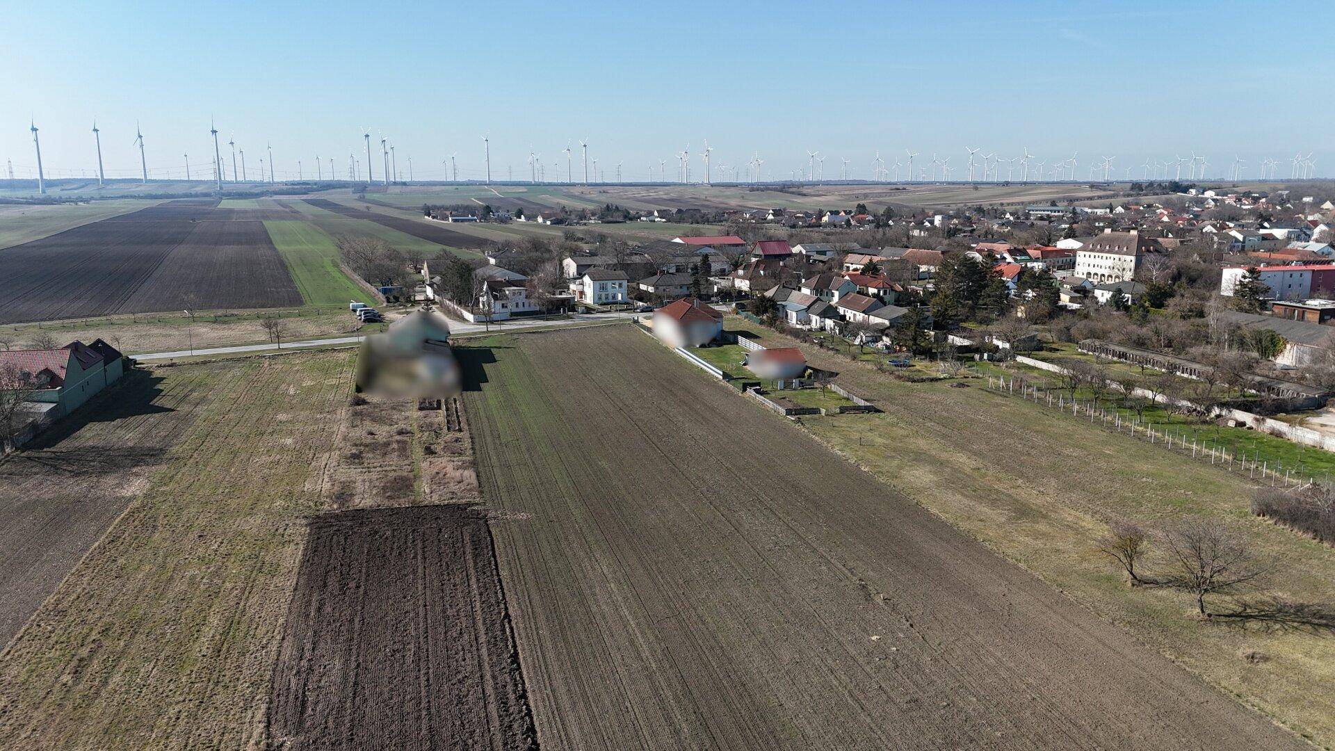 Weitläufige Luftaufnahme einer ländlichen Gegend mit Feldern, Siedlung und zahlreichen Windrädern.