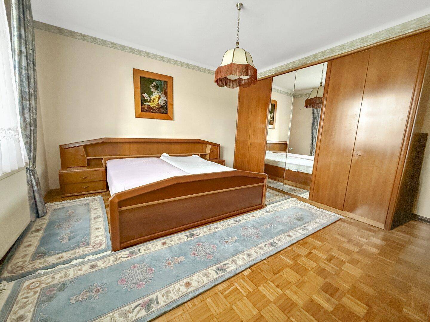 Schlafzimmer mit Doppelbett, Spiegelschrank und Parkettboden in einem traditionellen Einrichtungsstil.