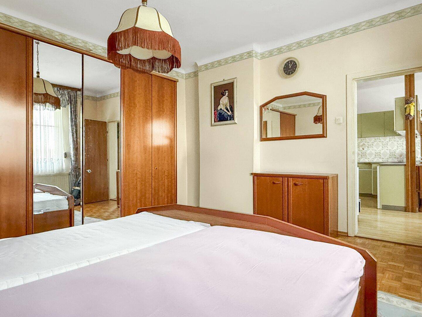 Schlafzimmer mit Doppelbett, Holzmöbeln und Blick in die angrenzende Küche, klassisch eingerichtet.
