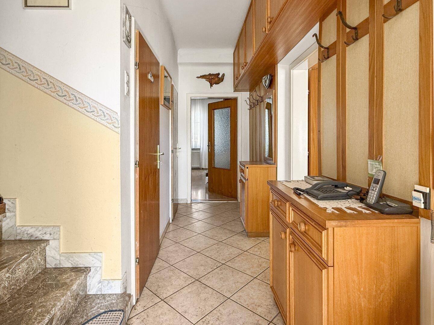 Heller Flur mit Fliesenboden, Holzmöbeln und Garderobe, der zu weiteren Räumen führt.