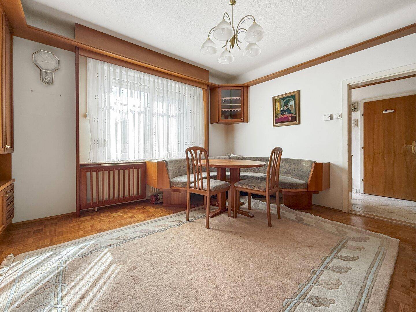 Wohnzimmer mit Essbereich, Holzeinbauten und großem Fenster, das viel Tageslicht hereinlässt.