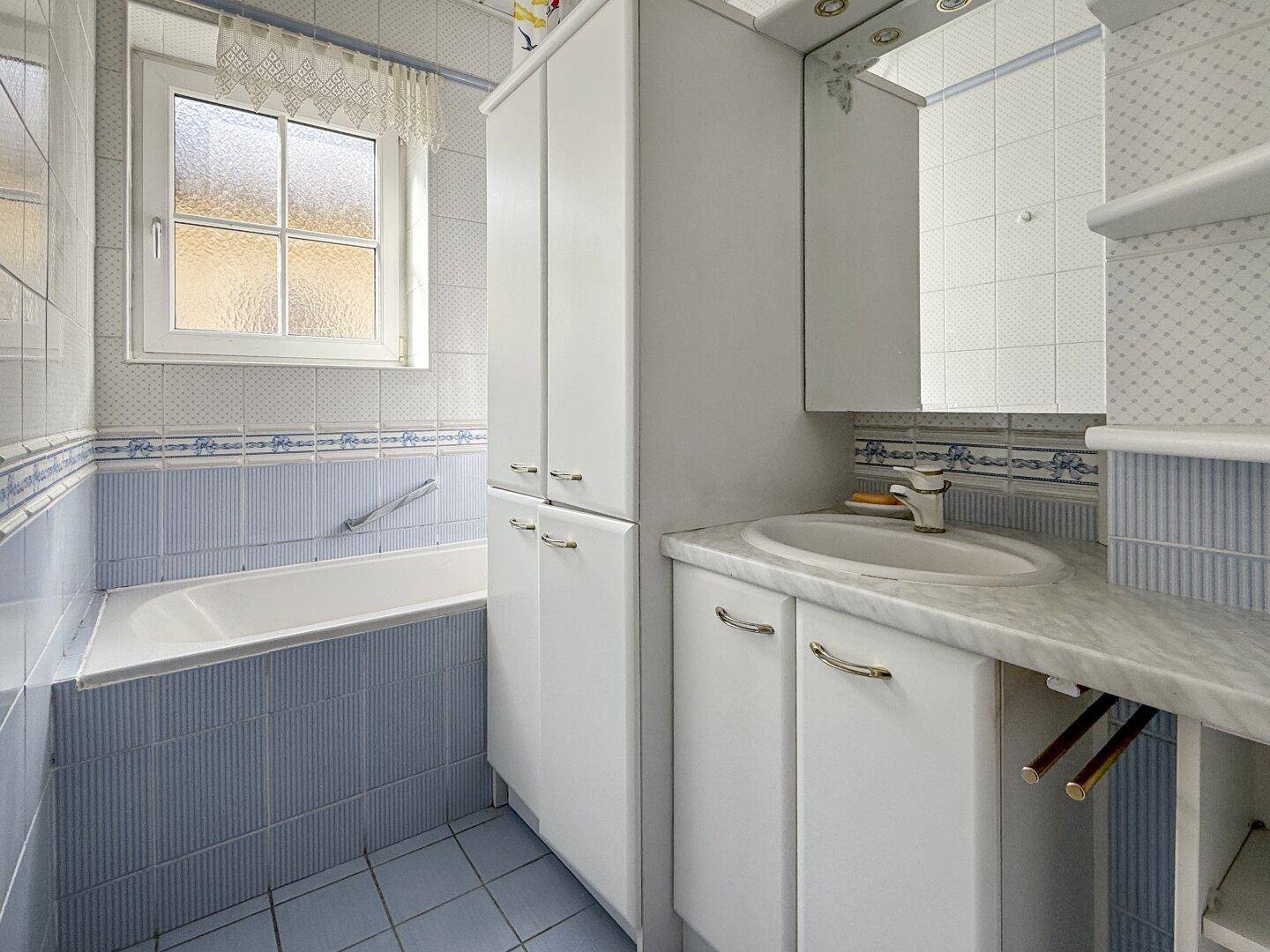 Badezimmer mit Badewanne, Fenster und blauen Fliesen, das eine helle und funktionale Umgebung bietet.