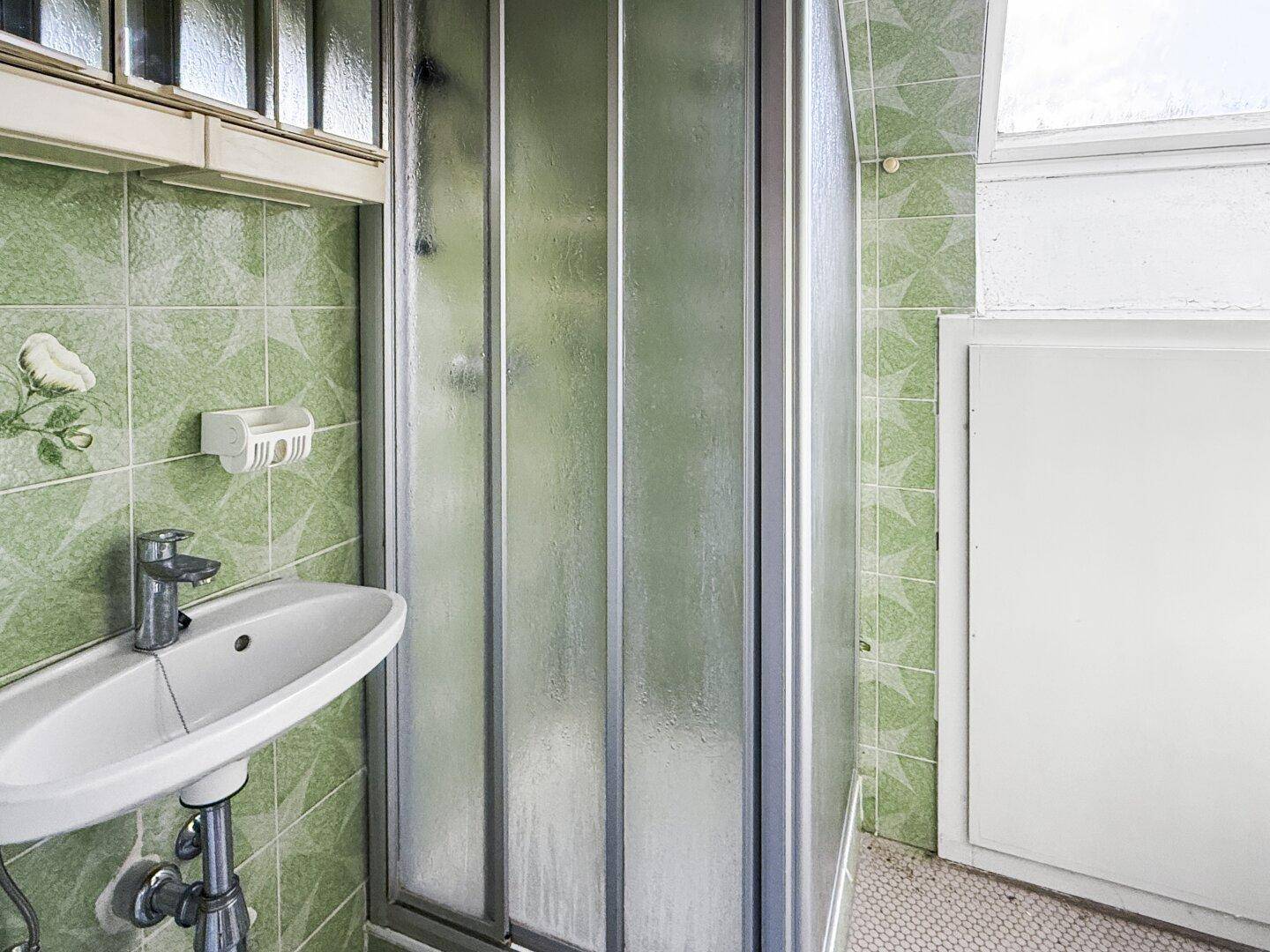 Kleines Badezimmer mit Dusche, grünen Fliesen und Waschbecken, funktional und hell.