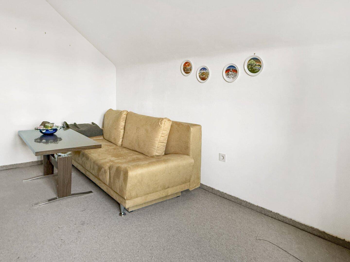 Helles Wohnzimmer im Dachgeschoss mit Schrägen, Sofa und Teppichboden, einfach eingerichtet.