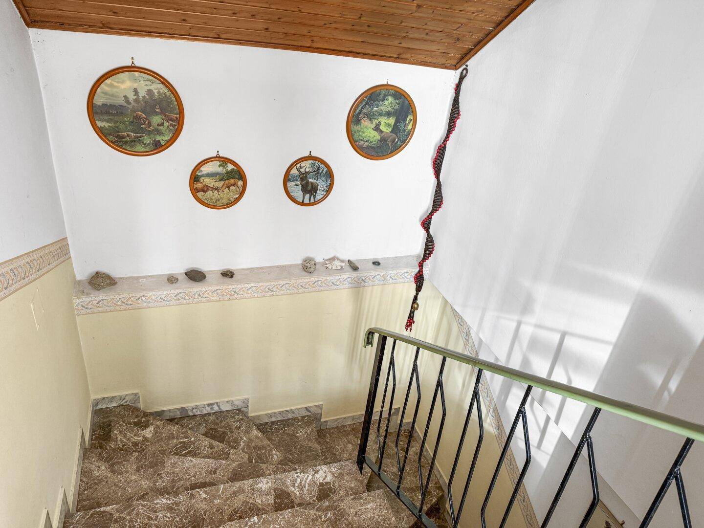 Treppenhaus mit Marmorstufen, Holzdecke und traditionellen Wanddekorationen, die zum Obergeschoss führen.
