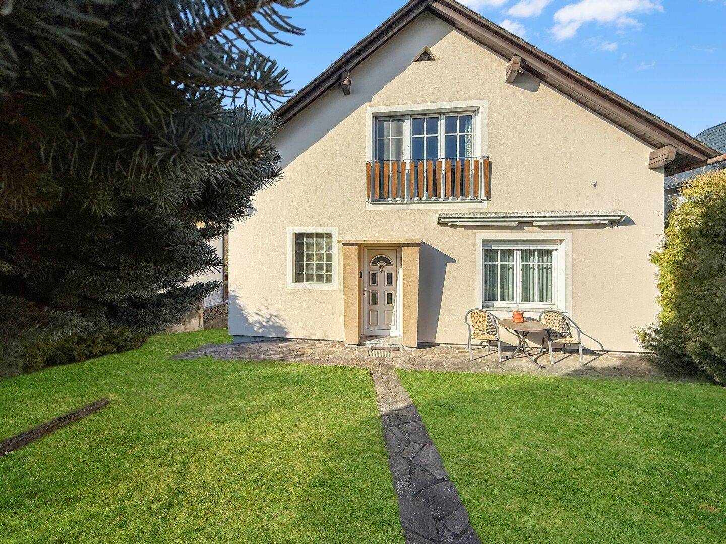 Einfamilienhaus mit gepflegtem Vorgarten, Steinweg und kleiner Sitzgelegenheit.