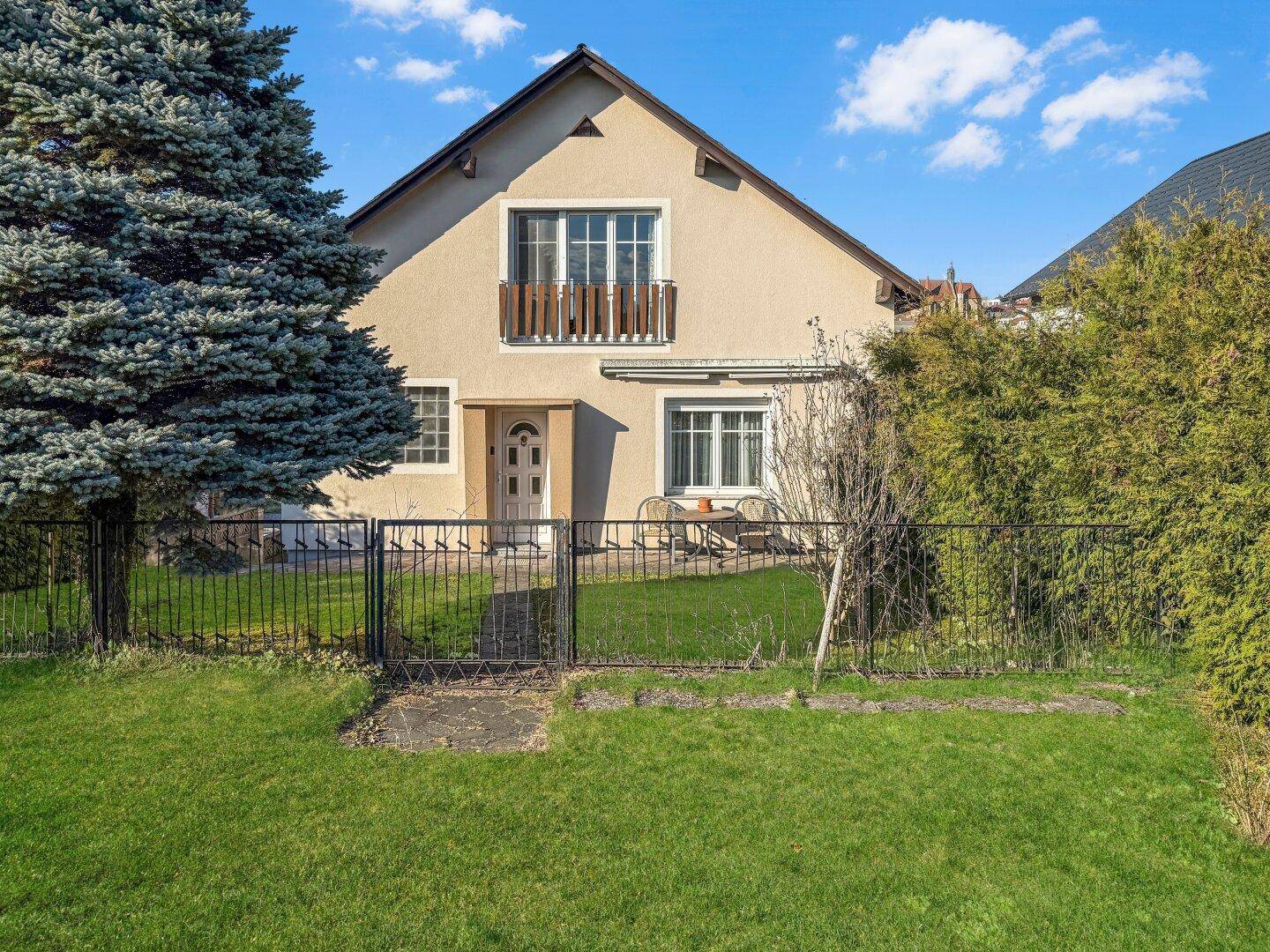 Einfamilienhaus mit gepflegtem Vorgarten, Rasenfläche und Zaun.