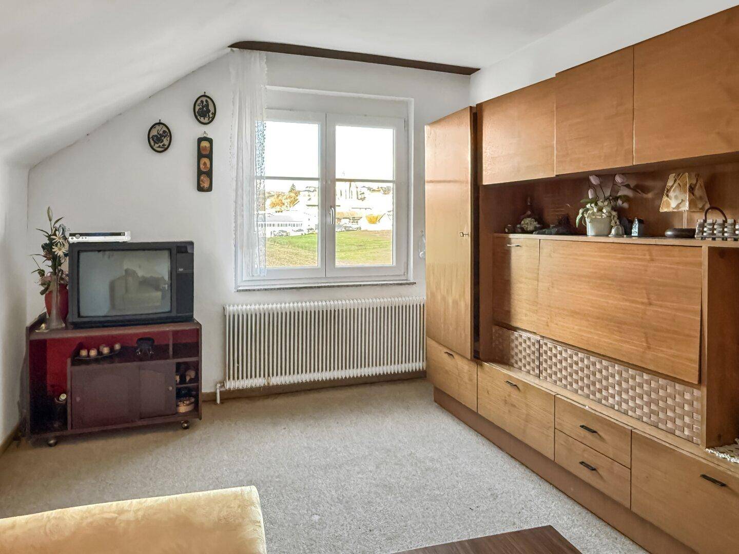 Dachzimmer mit Dachschräge, Fenster und Einbauschrank.