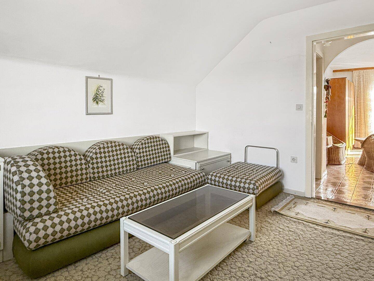 Dachzimmer mit Sofa, Couchtisch und Zugang zu einem weiteren Raum.