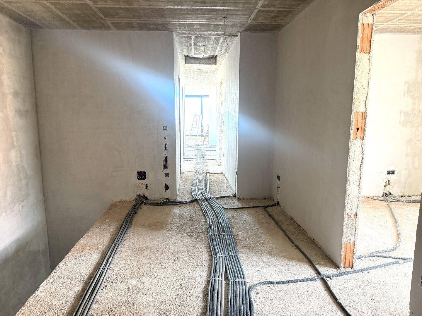 Innenraum im Rohbau mit sichtbaren Elektroinstallationen und Betonboden.
