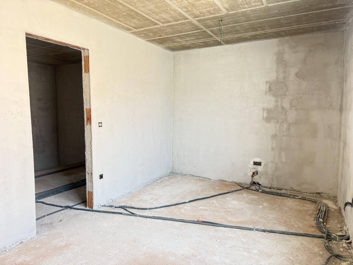 Unfertiger Raum im Rohbau mit Betonboden und vorbereiteten Wänden.