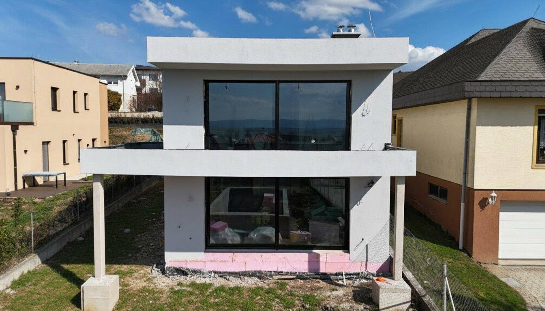 Neubau-Villa im Rohbau mit großen Fensterfronten und Balkon im Obergeschoss.