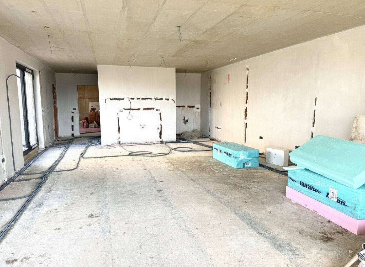 Großer offener Raum im Rohbau mit vorbereiteten Installationen und Blick nach draußen.