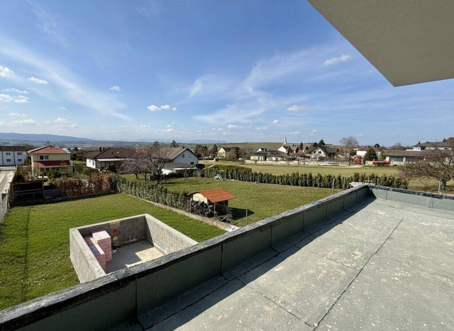Weitläufiger Blick über die ländliche Umgebung mit Gärten und Häusern unter blauem Himmel.
