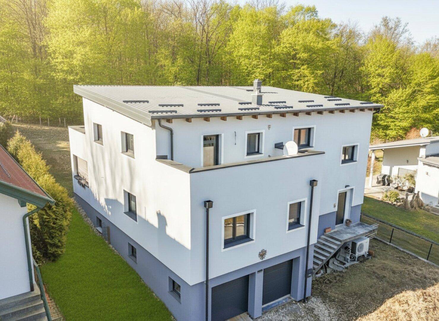 Ansicht des modernen Hauses mit weißer Fassade, dunklen Fenstern und integrierter Doppelgarage.