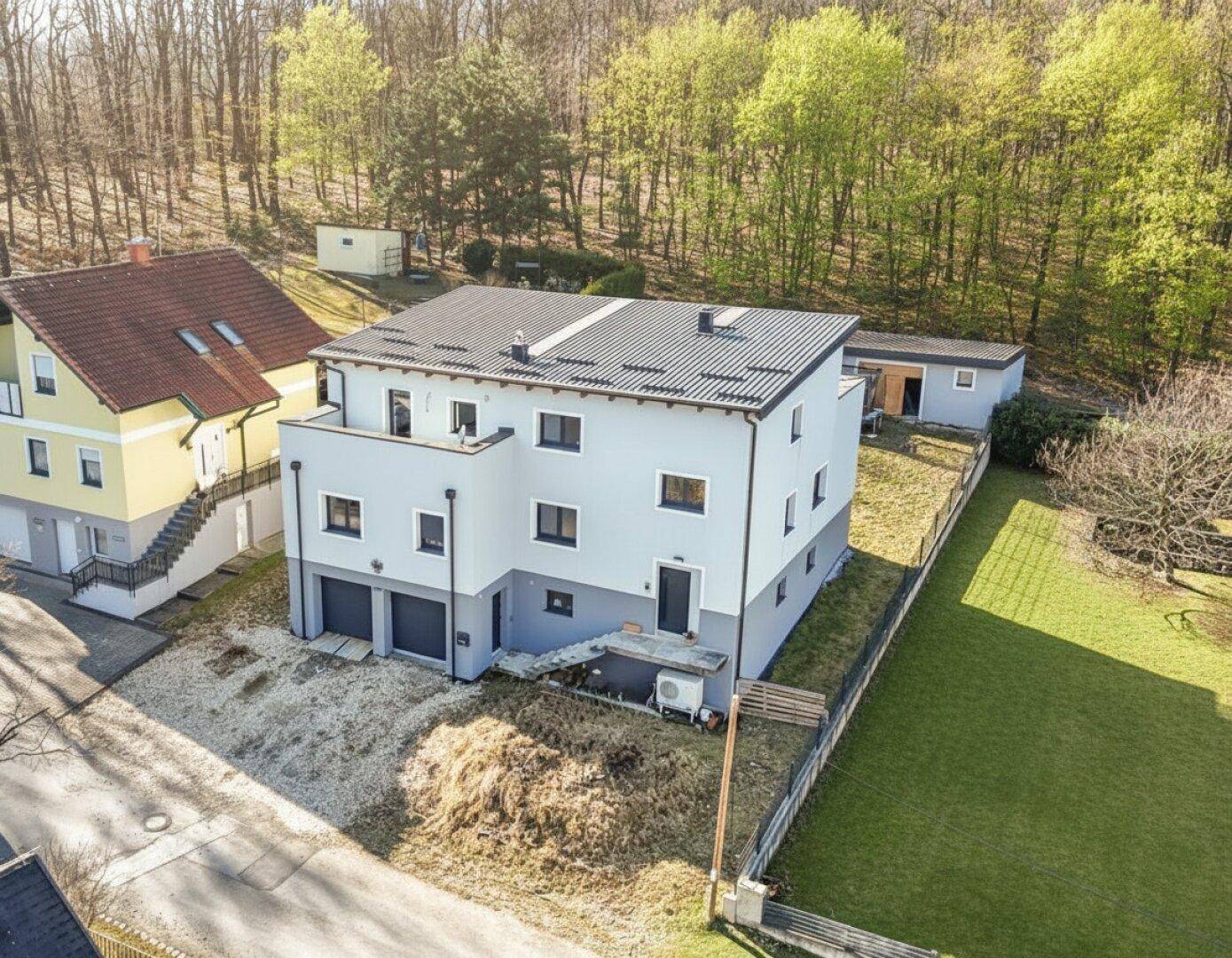 Luftaufnahme des modernen Hauses mit Garten, Garage und angrenzendem Waldgebiet.