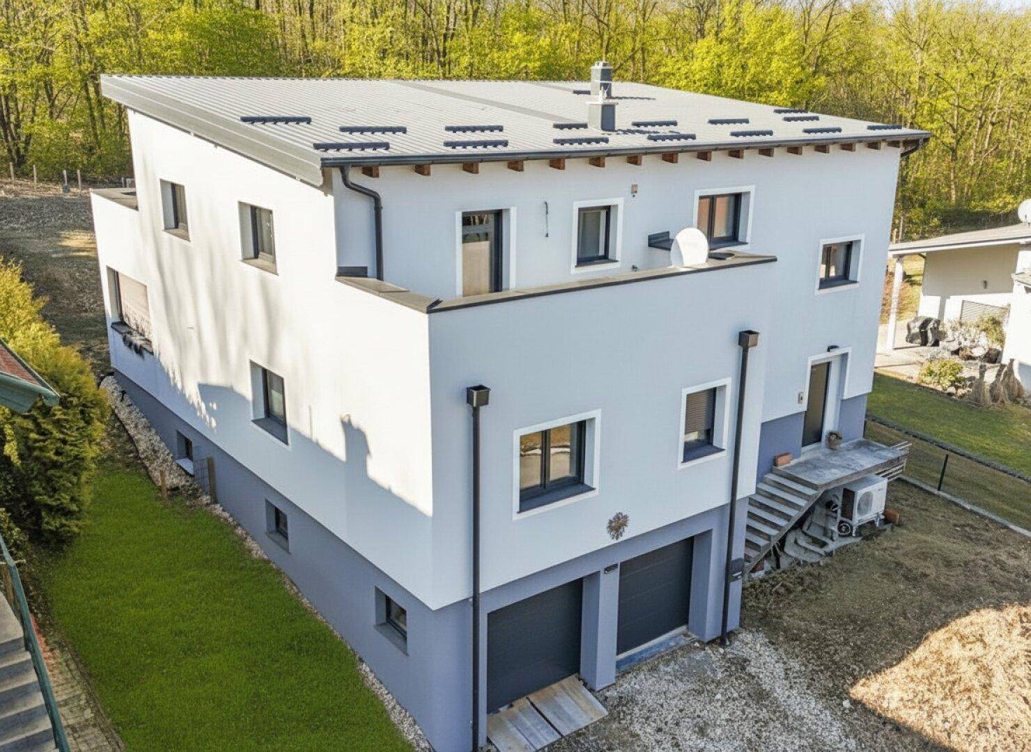 Modernes Einfamilienhaus mit Flachdach, Doppelgarage und Blick auf die umliegende Natur.