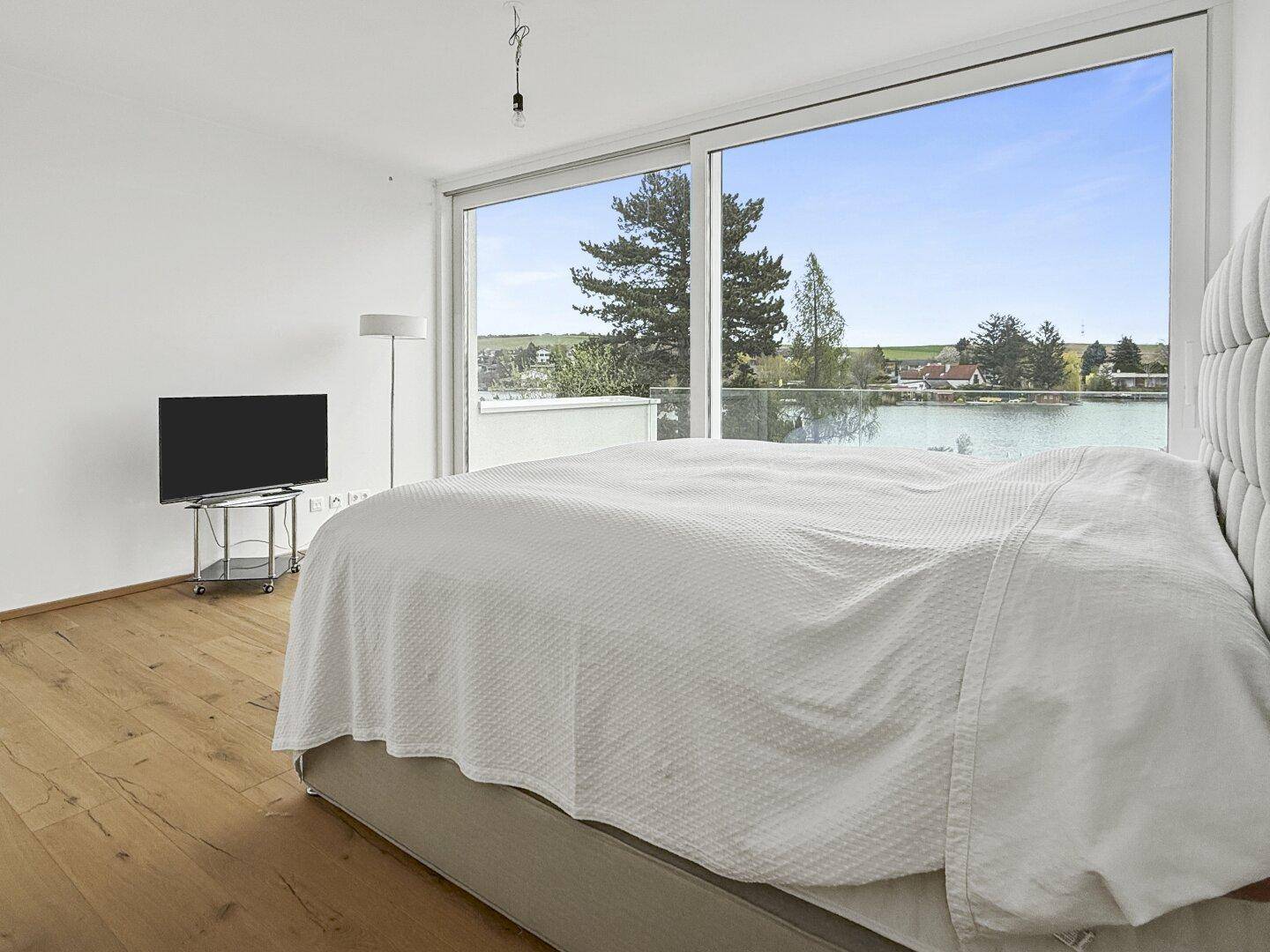 Helles Schlafzimmer mit Seeblick, Holzboden und moderner Einrichtung.