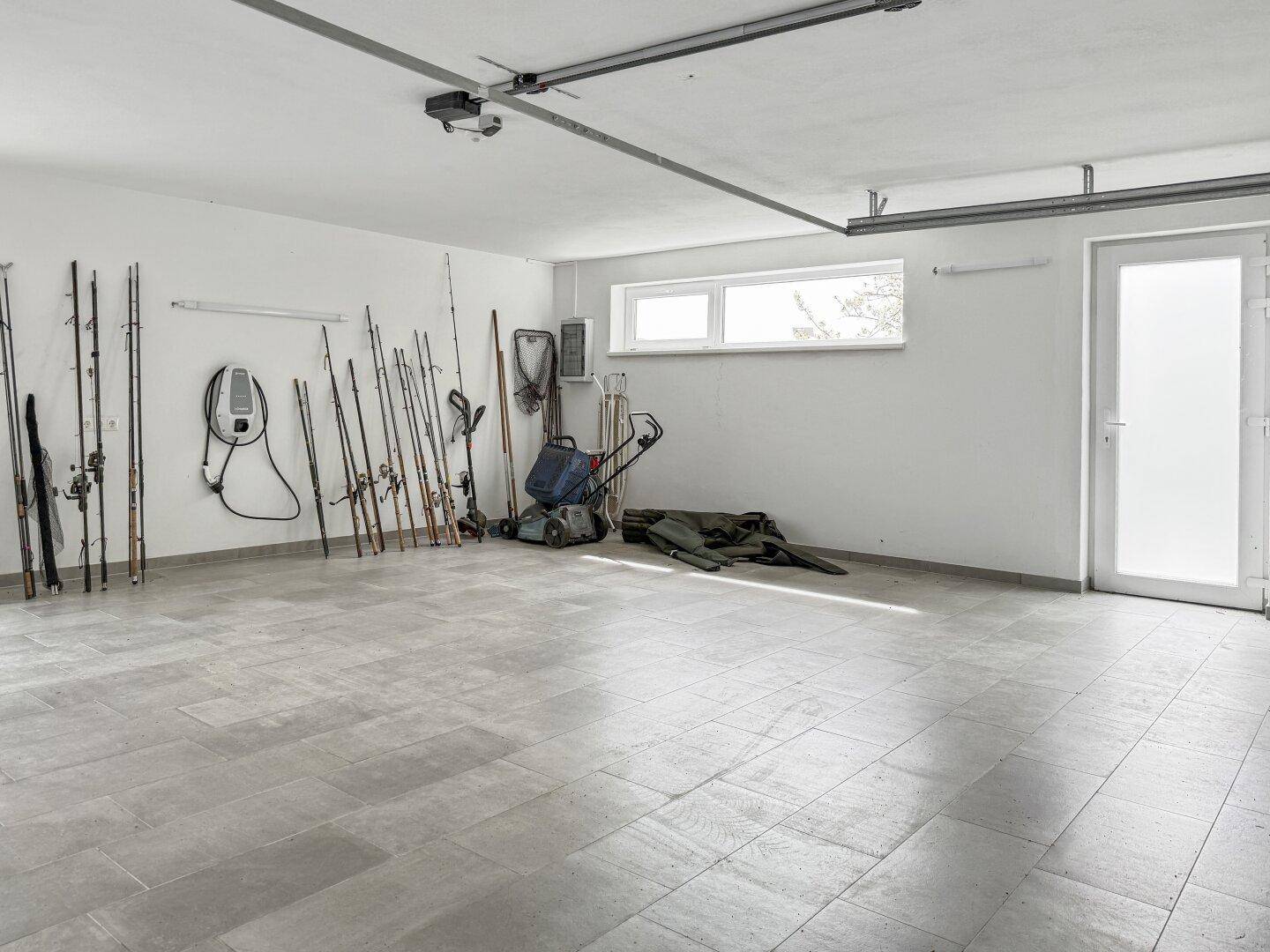 Geräumige Garage mit Fliesenboden, Fenster und Ladestation für Elektrofahrzeuge.