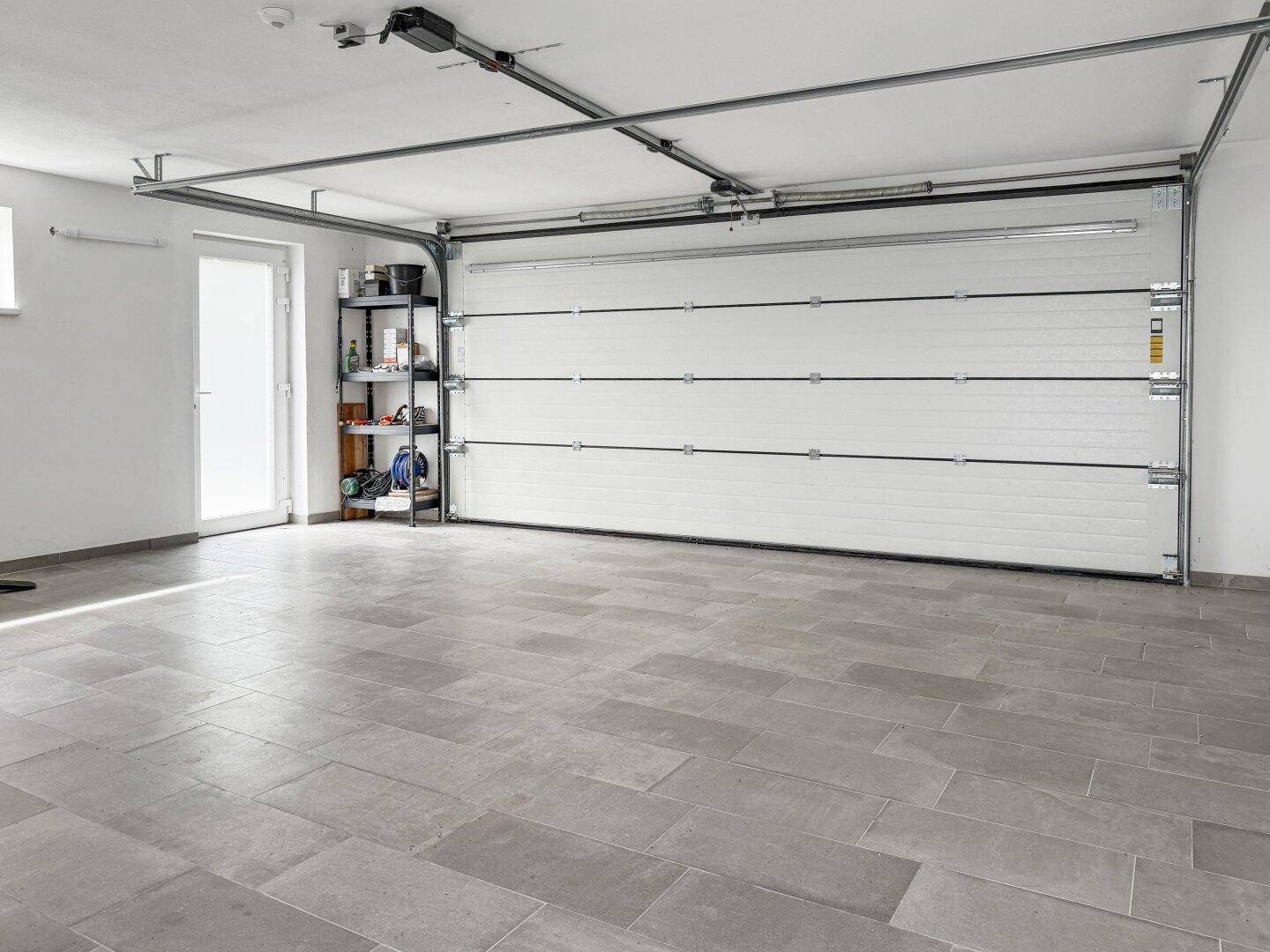 Geräumige Garage mit Fliesenboden und automatischem Garagentor.