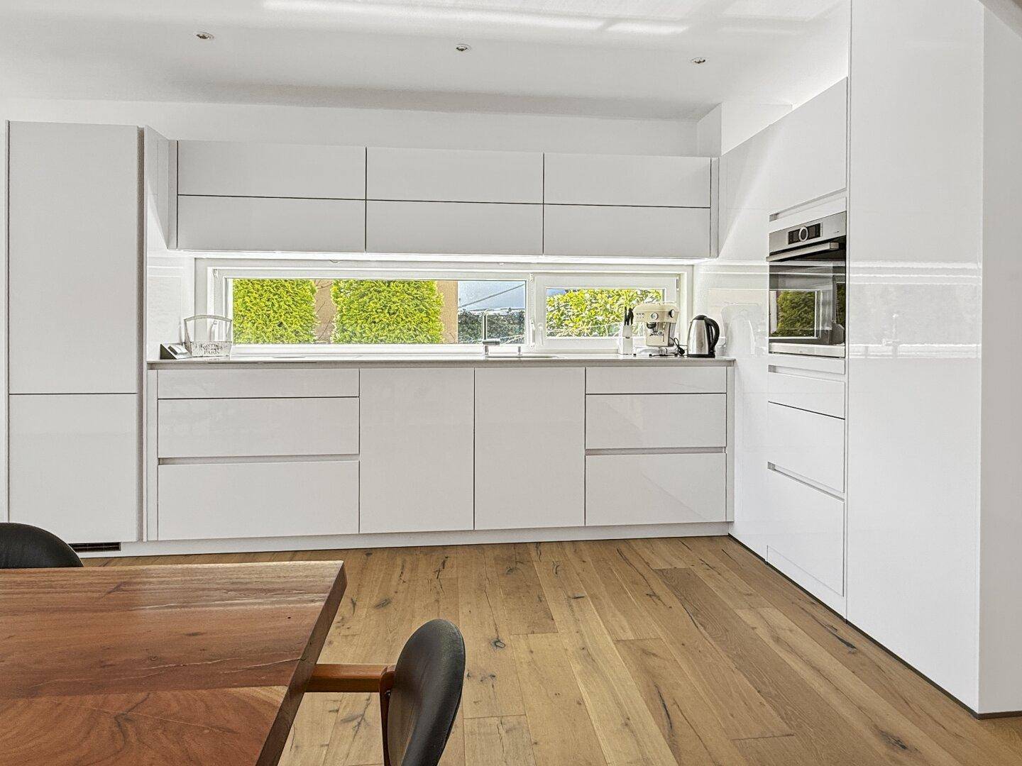 Moderne Einbauküche mit weißen Hochglanzschränken, integrierten Geräten und Fenster.
