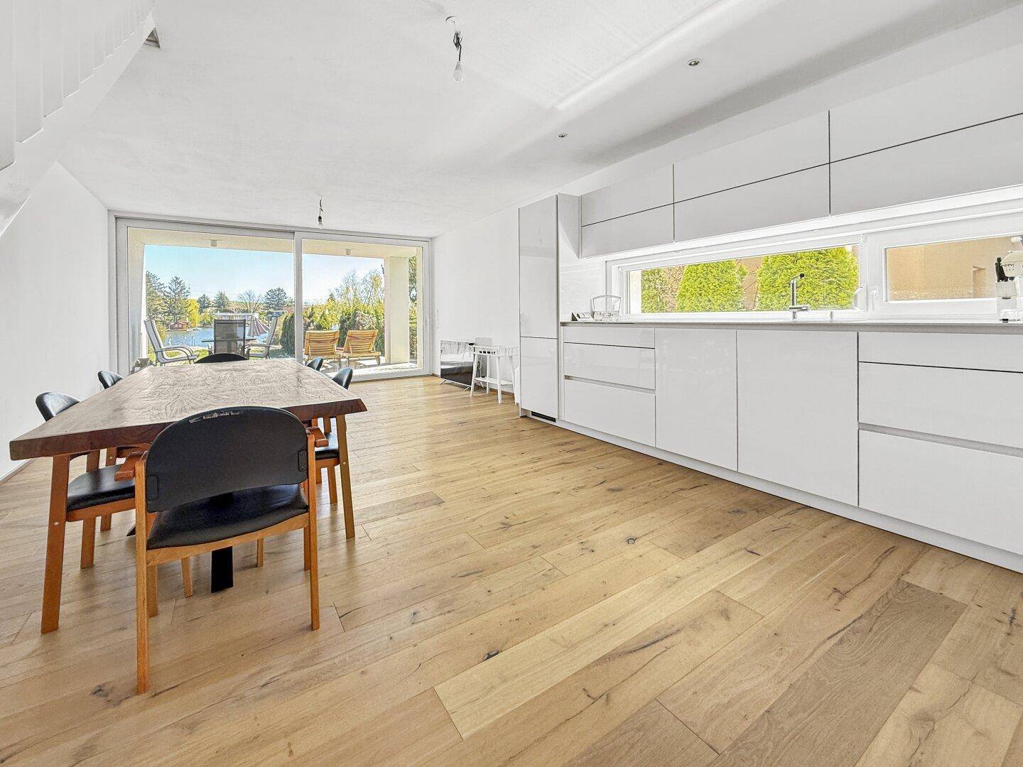 Offene Küche mit weißen Hochglanzfronten, Holzboden und Zugang zur Terrasse.