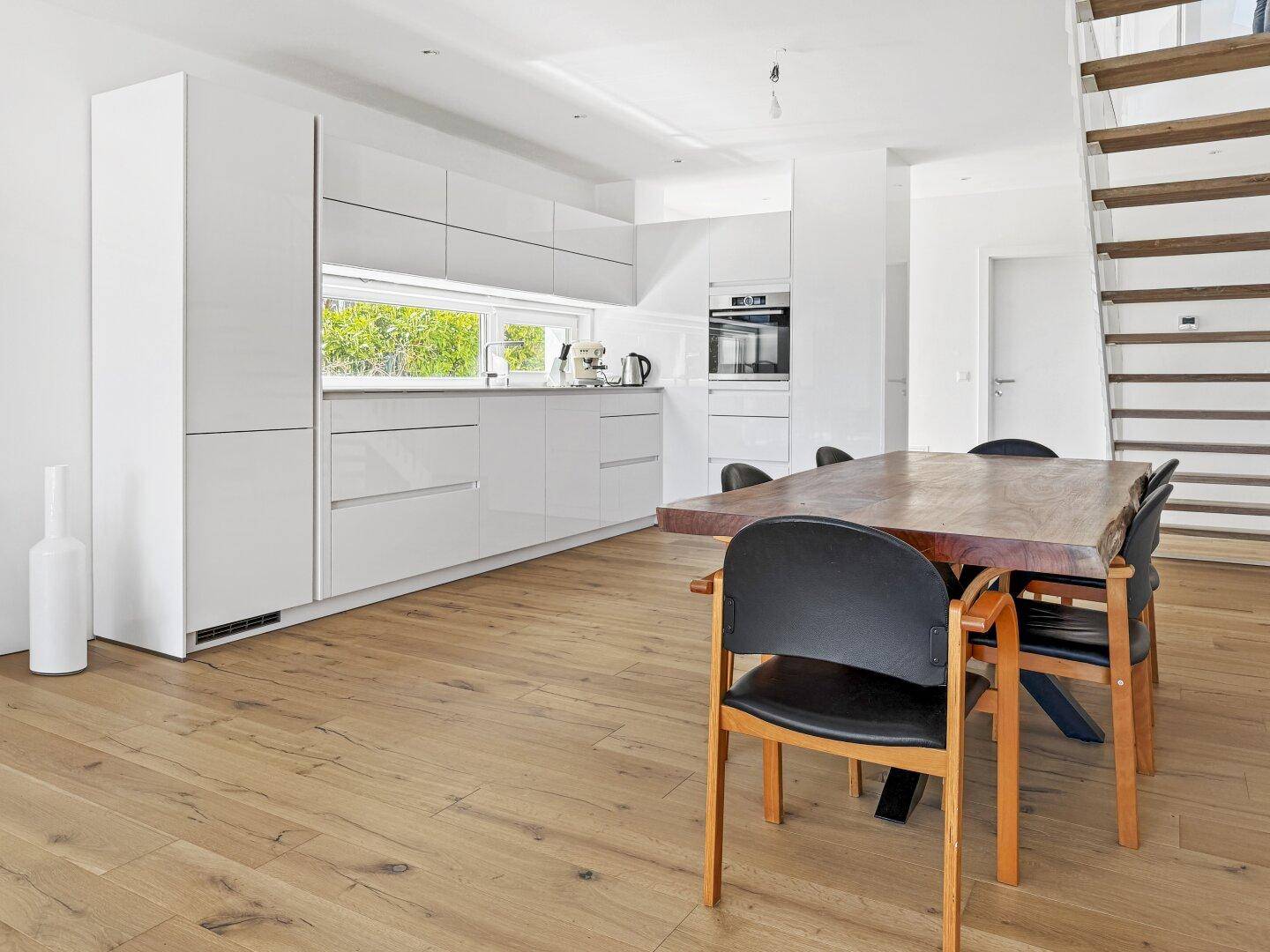 Helle offene Küche mit Esstisch, Holzboden und modernen weißen Schränken.