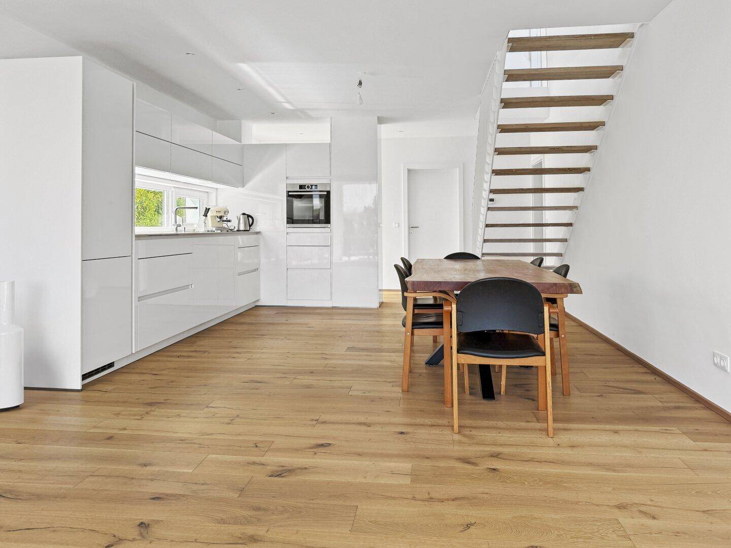 Geräumige offene Küche mit Essbereich, Holzboden und modernen weißen Einbaumöbeln.