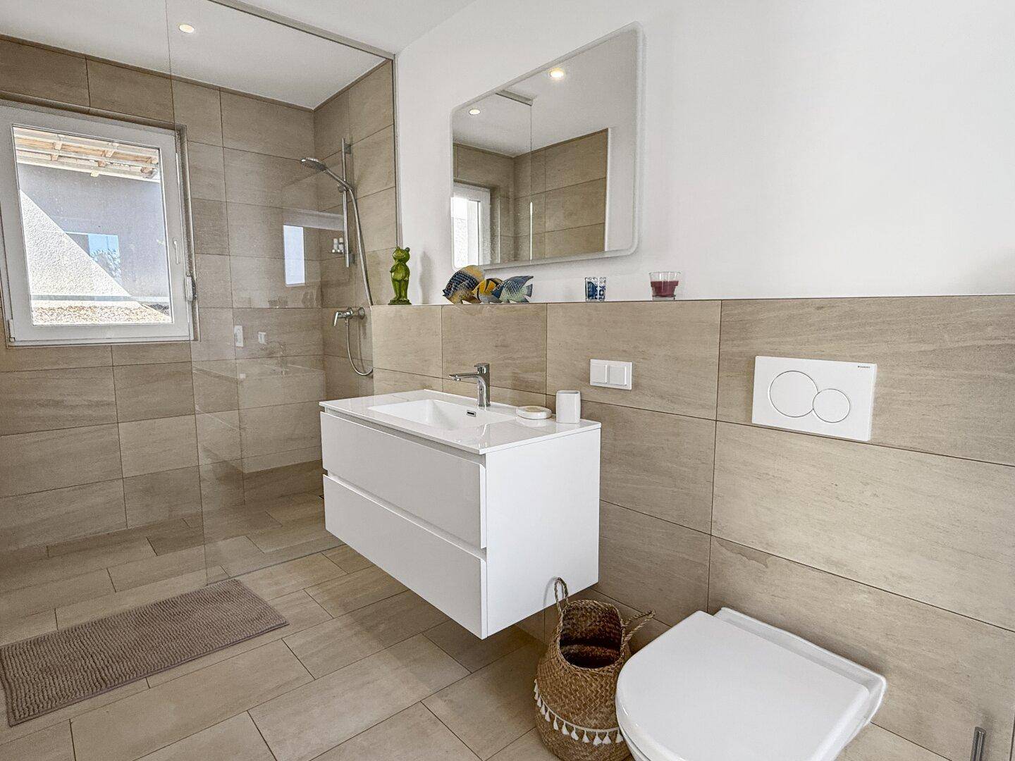 Modernes Badezimmer mit beigefarbenen Fliesen, bodengleicher Dusche und Fenster.