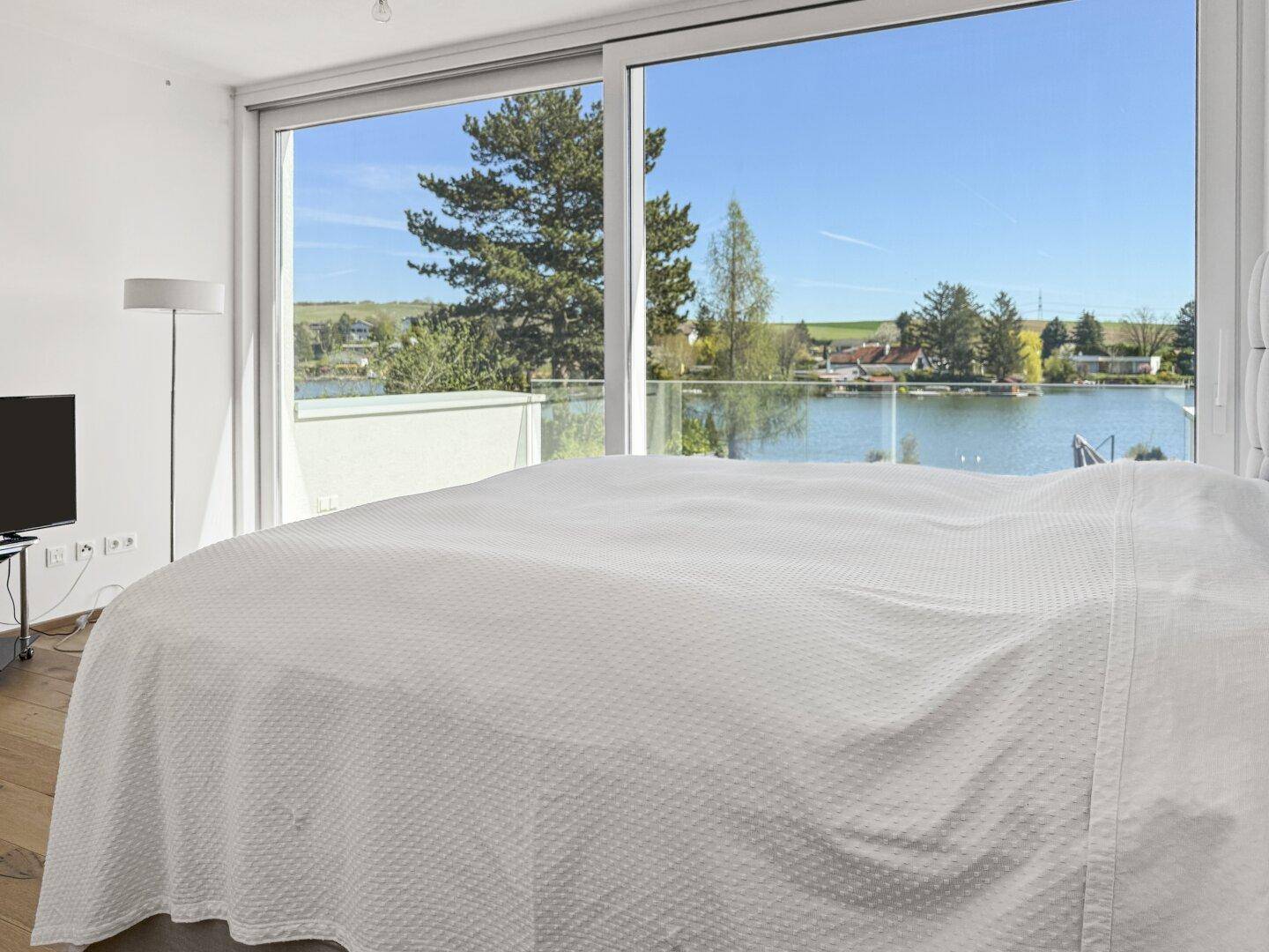 Helles Schlafzimmer mit Seeblick, Holzboden und moderner Einrichtung.