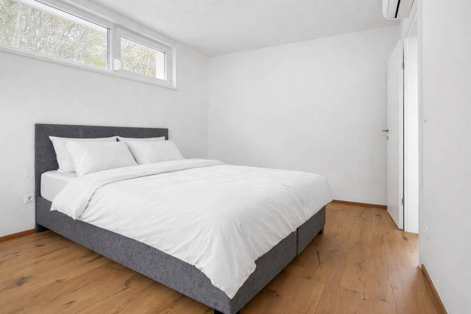 Helles Schlafzimmer mit Holzboden, weißen Wänden und Klimaanlage.