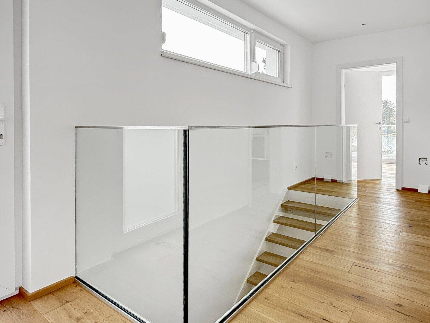 Heller Flur im Obergeschoss mit Glasgeländer und Holzboden.