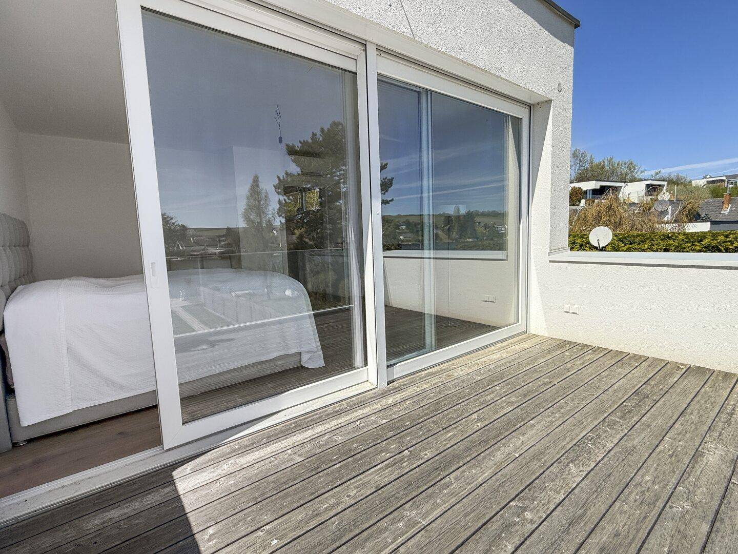 Geräumiger Holzbalkon mit Zugang vom Schlafzimmer und Blick auf die Umgebung.