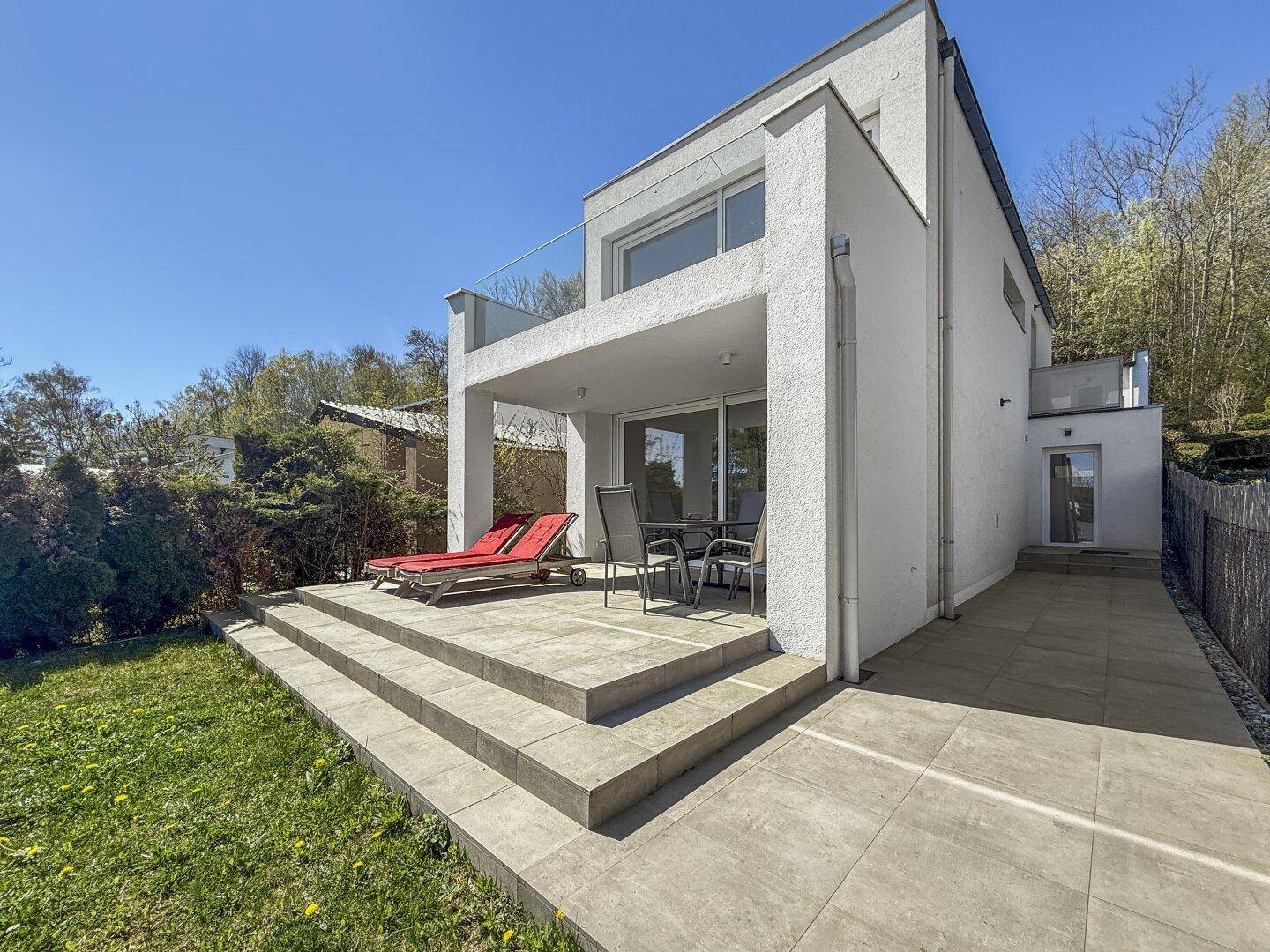 Sonniger Terrassenbereich mit Liegestühlen und Zugang zum Garten.